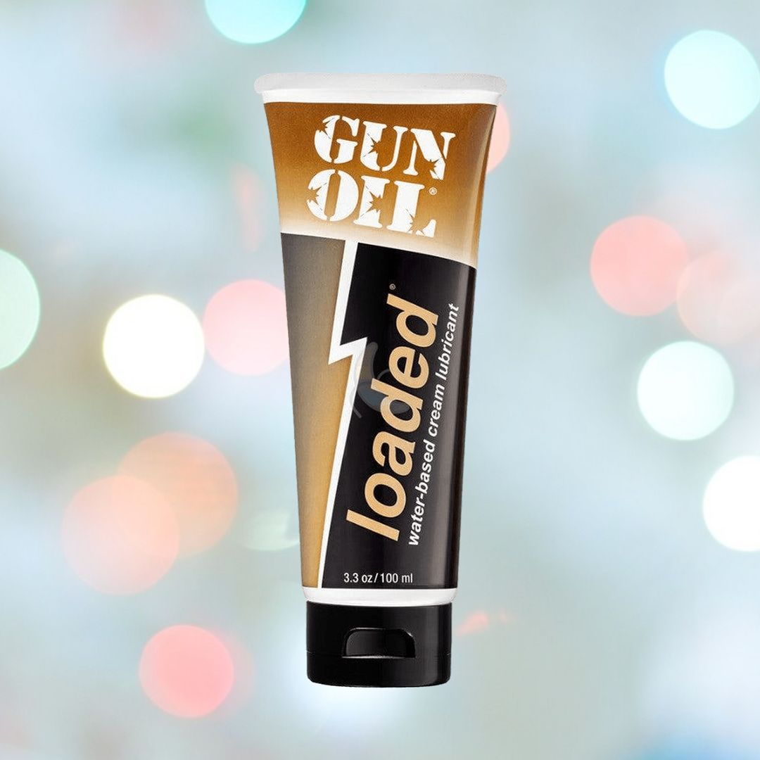 A tube of Gun Oil "Force Loaded" Hybrid Lube, 3.3 oz (100 ml), is shown against a soft background with bokeh lights. The tube has a brown and white design with bold text, paired with a leak-proof pump bottle for convenience.