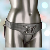 A close-up image shows the lower torso of a mannequin wearing CalExotics' Her Royal Harness The Regal Empress Pewter, a black, textured, strappy vegan leather harness with interchangeable ring details. The background features a soft bokeh effect with pastel blue and pink hues.