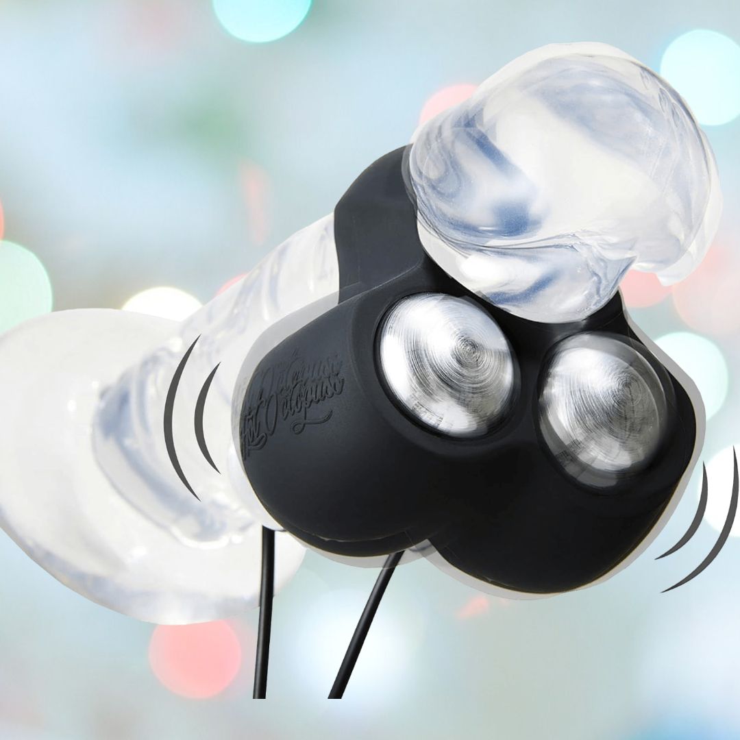 A clear, textured gadget resembling the Hot Octopuss Jett - Vibrating C-Ring with Remote Control showcases a black section equipped with multiple lenses and cords extending from its base. The softly blurred background, filled with colorful lights, enhances the high-tech aesthetic. Illustrated vibrating motion lines surround the device.