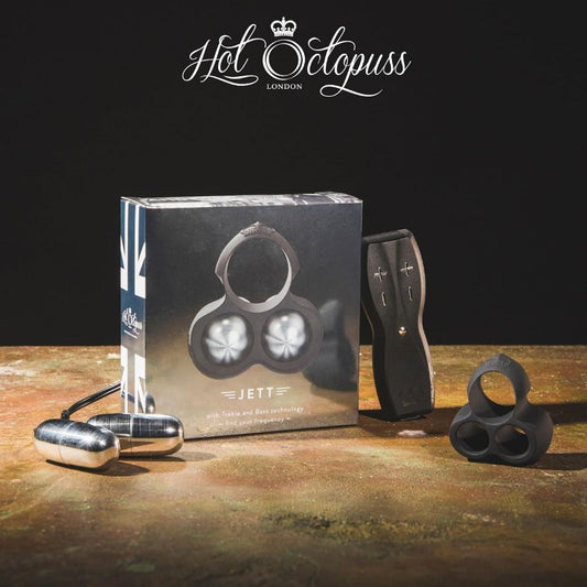 A box featuring the name "JETT" from Hot Octopuss is showcased next to the product, a vibrating C-ring with remote control designed for a hands-free orgasm experience. This personal massager includes metallic components and adjustable settings, with a strap accessory displayed on the right. 1080