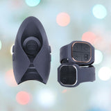 Close-up of a black wireless earpiece with a sleek design next to two Hot Octopuss Pulse DUO LUX couples vibrators, featuring buttons and a vibrating base, set against a blurred background with colorful bokeh lights.