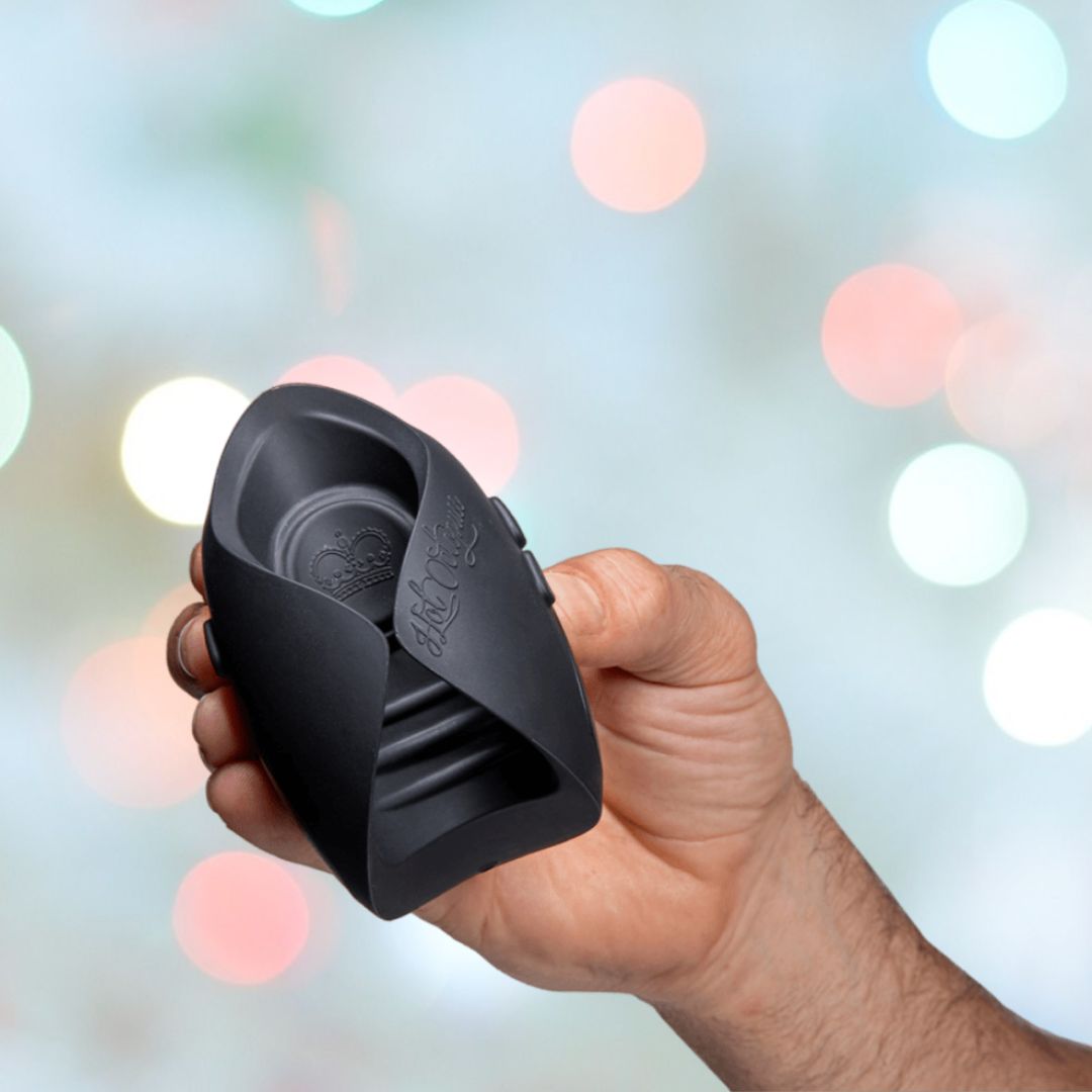 A person is holding the Hot Octopuss Pulse Solo Essential, a black, curved electronic device, set against a backdrop of colorful, blurred lights. This male vibrating masturbator features Pulse Plate technology and includes a textured grip with side buttons and engraved text on the front.