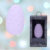 A lilac Je Joue Mimi Deux Pebble Vibrator is showcased beside its matching Je Joue box, set against a background of soft, colorful blurred lights that enhance the calming ambiance of its low-frequency motor.