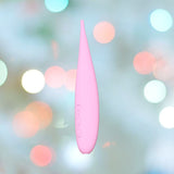 A pink LELO DOT Travel Clitoral Pinpoint Vibrator, featuring a sleek teardrop shape and equipped with Infinite Loop Technology and three buttons on the side, is set against a softly focused backdrop of colorful, round bokeh lights, evoking a playful and dreamy atmosphere.