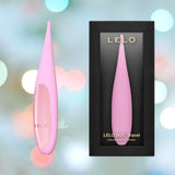 A LELO DOT Travel Clitoral Pinpoint Vibrator in pink, featuring the innovative Infinite Loop Technology, sits beside its sleek black and pink retail box labeled "LELO DOT Travel Clitoral Pinpoint Vibrator Pink," set against a dreamy backdrop of pastel bokeh lights.