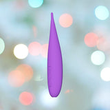 The LELO DOT Travel Clitoral Pinpoint Vibrator Purple, a personal care device with buttons, is showcased against a soft-focus backdrop of pastel-colored lights. This chic travel companion from LELO boasts Infinite Loop Technology for limitless possibilities.