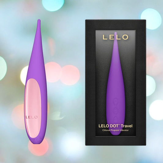 The LELO DOT Travel Clitoral Pinpoint Vibrator in purple is elegantly presented next to its sleek black box packaging. The backdrop of soft, colorful bokeh lights highlights its appeal as an ideal travel companion. 1080