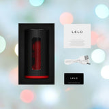 The latest innovation, the LELO F1S V3 Male Masturbator Red, is displayed as a sleek black cylindrical device featuring a striking red interior, elegantly positioned in an open rectangular box. Accompanying it are a USB charging cable, warranty registration card, and instruction booklet. The scene is set against a backdrop adorned with vibrant, blurred lights echoing the essence of smart technology.