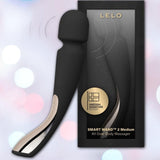 The LELO Smart Wand 2 Medium Personal Wand Massager by LELO in black is displayed beside its box, which features a gold emblem and product name. Soft, blurred pastel lights in the background highlight this stylish waterproof wand.