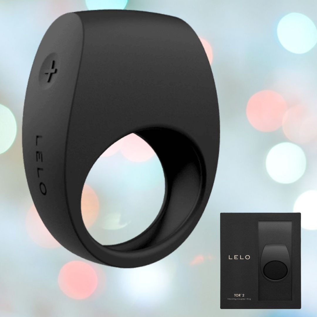 The LELO Tor 2 Vibrating Cock Ring - Black showcases a smooth, modern design with a "+" button on the side. Crafted from premium silicone material, the brand name "LELO" is prominently displayed on the ring. The product packaging is presented to the right against a softly blurred, colorful background.