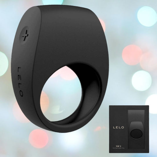 The LELO Tor 2 Vibrating Cock Ring - Black showcases a smooth, modern design with a "+" button on the side. Crafted from premium silicone material, the brand name "LELO" is prominently displayed on the ring. The product packaging is presented to the right against a softly blurred, colorful background. 1080