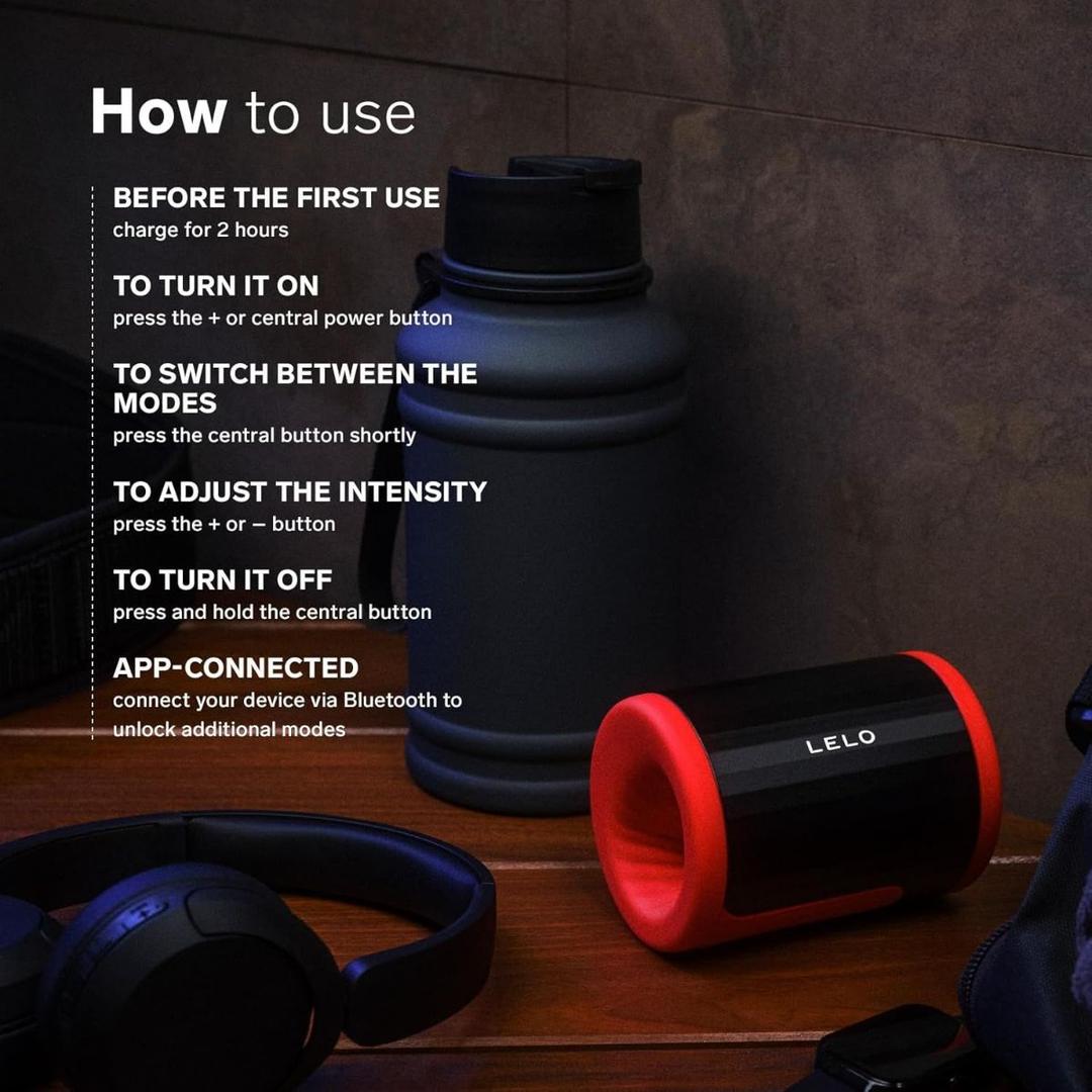 A black and red LELO F2S Massager & Stroker Red by LELO rests on a dark surface next to a water bottle and headphones, with usage instructions for this app-controlled masturbator shown in white text on the image.