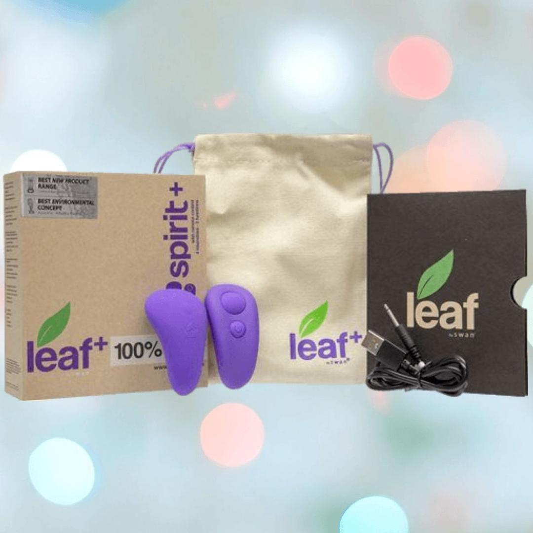 Two BMS Leaf + Spirit Panty Vibes in purple, a beige drawstring pouch, cardboard packaging, a USB charging cable, and a black card with a green leaf logo are shown against a softly blurred background with colorful lights.
