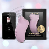 The LELO Sona 3 Cruise - Soft Pink, a sonic clitoral massager from LELO, is shown alongside its black box and a smartphone displaying the app interface, set against a softly blurred background with pastel circles.