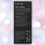 Purple LELO AKO™ Originals rectangular box with white text showing waterproof vibrator features in English and Spanish, legality icons, and company details, displayed on a softly blurred pastel pink and blue background.