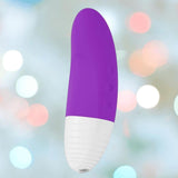 The LELO Lelo AKO Originals Purple is a curved, cylindrical purple and white personal massager with ribbed texture at one end and side control buttons, displayed against a blurred pastel light background.