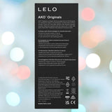 A purple product box labeled "LELO AKO Originals" with white feature text in several languages, displayed against a softly blurred background illuminated by pastel-colored lights.
