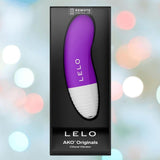 The LELO AKO Originals Purple clitoral vibrator by LELO is shown in its packaging, labeled as remote-controlled, against a blurred, colorful background.