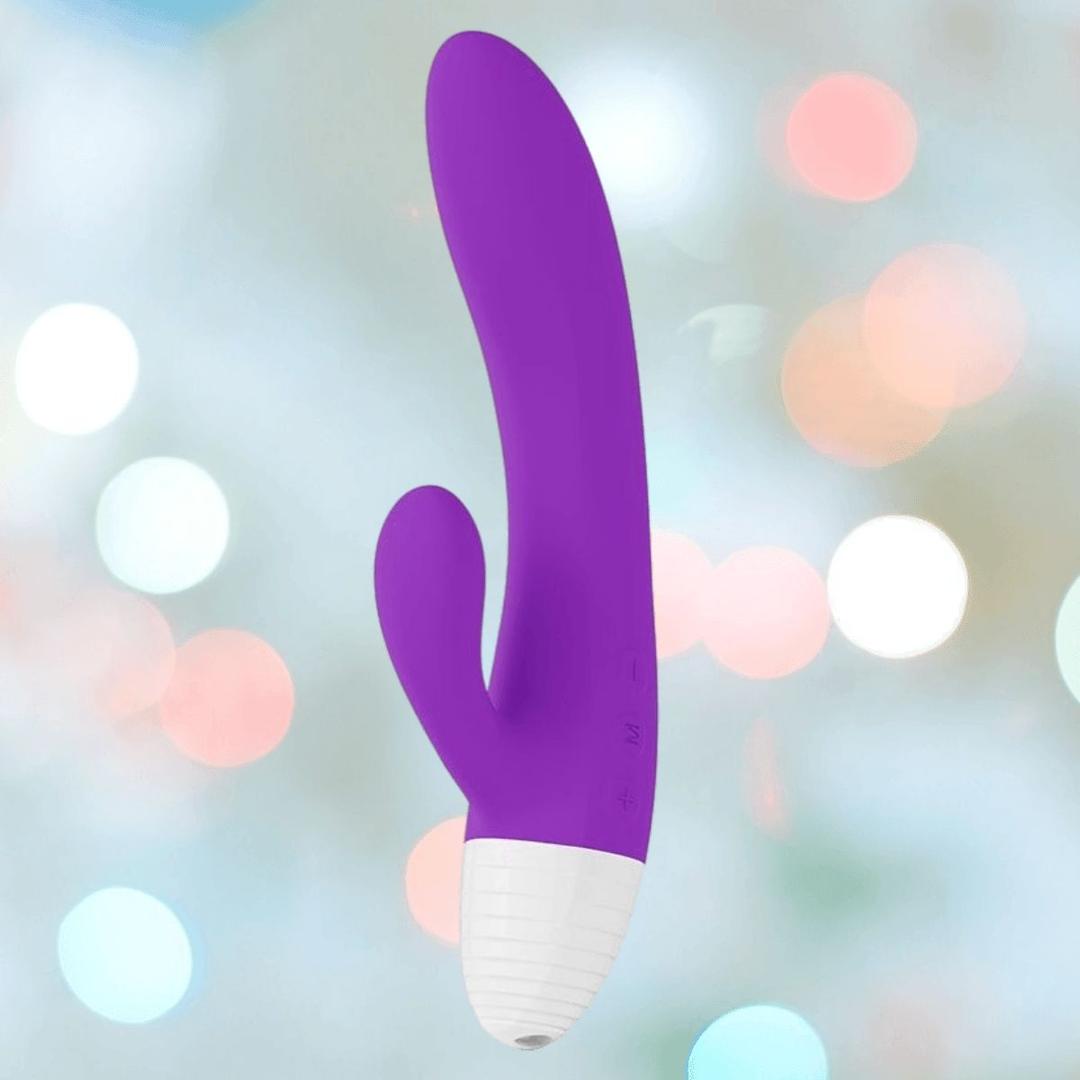 The LELO KAYA Originals Purple by LELO is a silicone vibrator with a white base, curved main shaft, and smaller extension, shown against a soft, blurred background with multicolored bokeh lights.