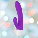 The LELO KAYA Originals Purple by LELO is a silicone vibrator with a white base, curved main shaft, and smaller extension, shown against a soft, blurred background with multicolored bokeh lights.