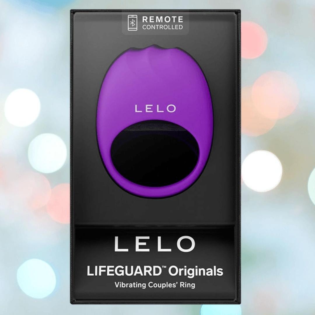 A boxed LELO LIFEGUARD Originals Purple vibrating couples’ ring with "REMOTE CONTROLLED" at the top, set against a blurred background of pastel lights.
