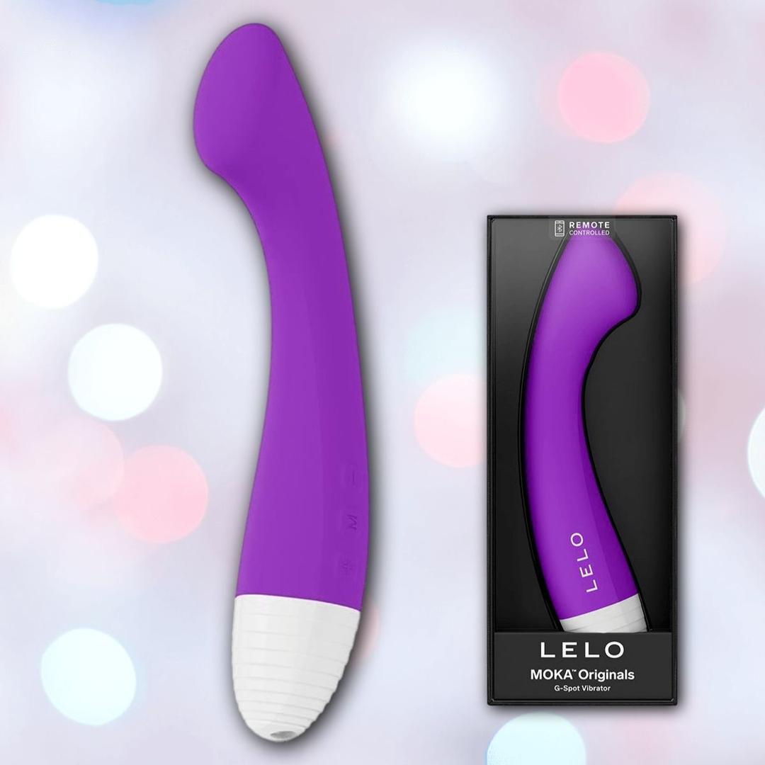 A Lelo MOKA Originals Purple G-spot vibe by LELO is displayed next to its black "LELO MOKA Originals" box, set against an out-of-focus pastel background.