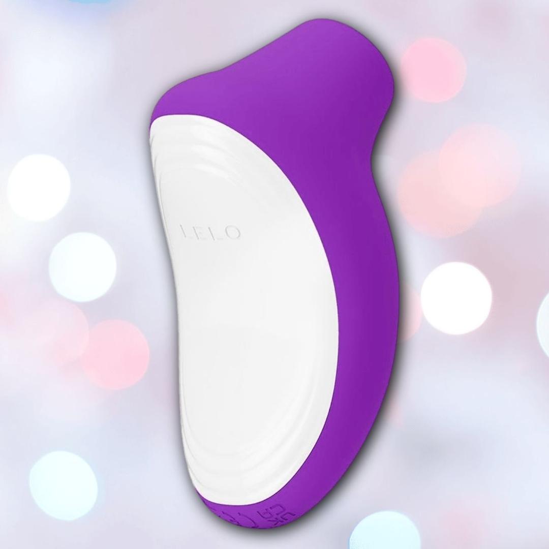 The LELO SONA Originals Purple, a handheld curved sonic massager with a smooth surface, is photographed against a soft, pastel bokeh background.