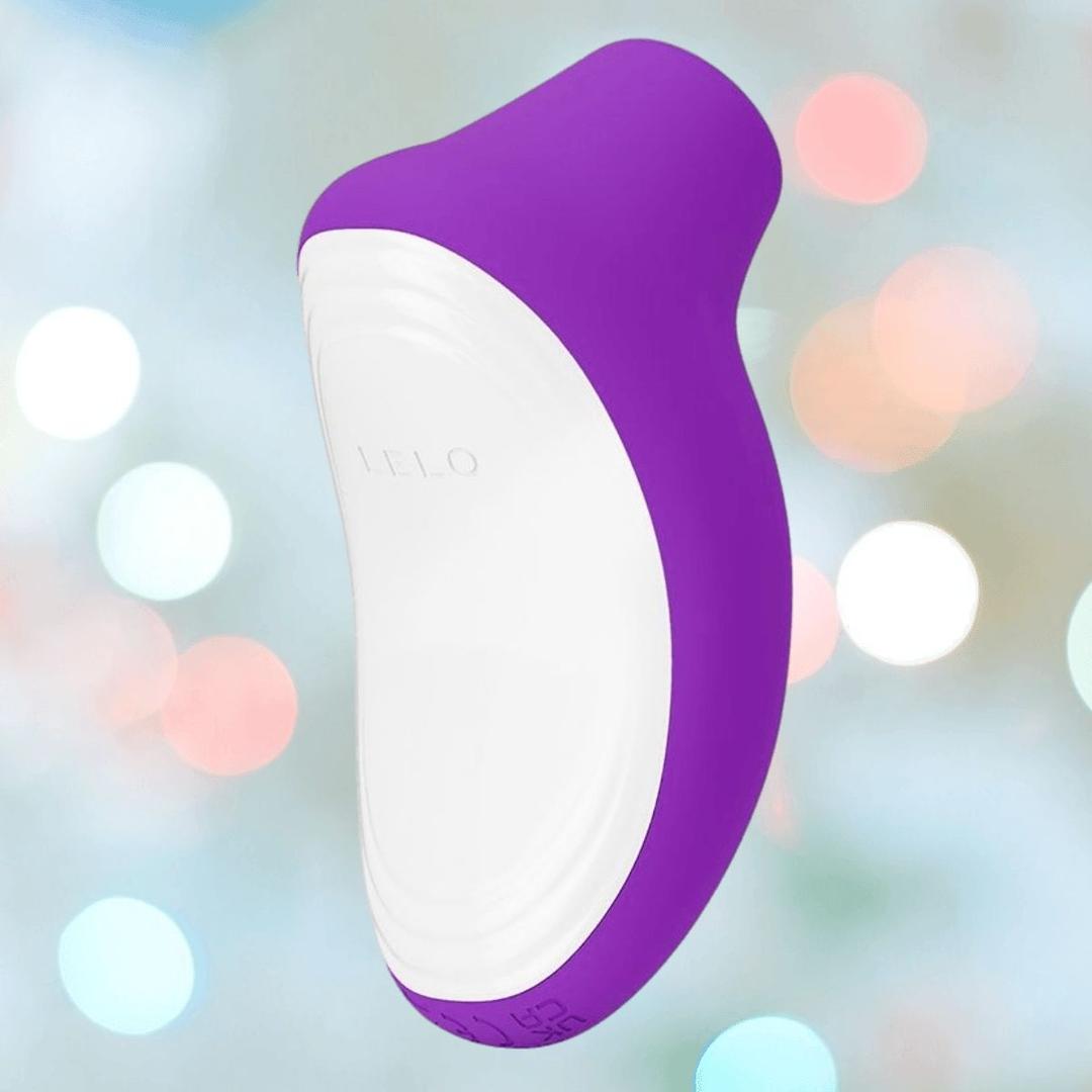 The LELO SONA Originals Purple is a white and purple silicone handheld device with an ergonomic, curved shape and "LELO" embossed on its surface, shown floating against a blurred backdrop of pastel lights.