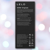Purple product packaging for LELO SONA™ Originals by LELO with white text, product description, and technical details for this sonic massager, set against a blurred background with soft pink, white, and blue bokeh lights.