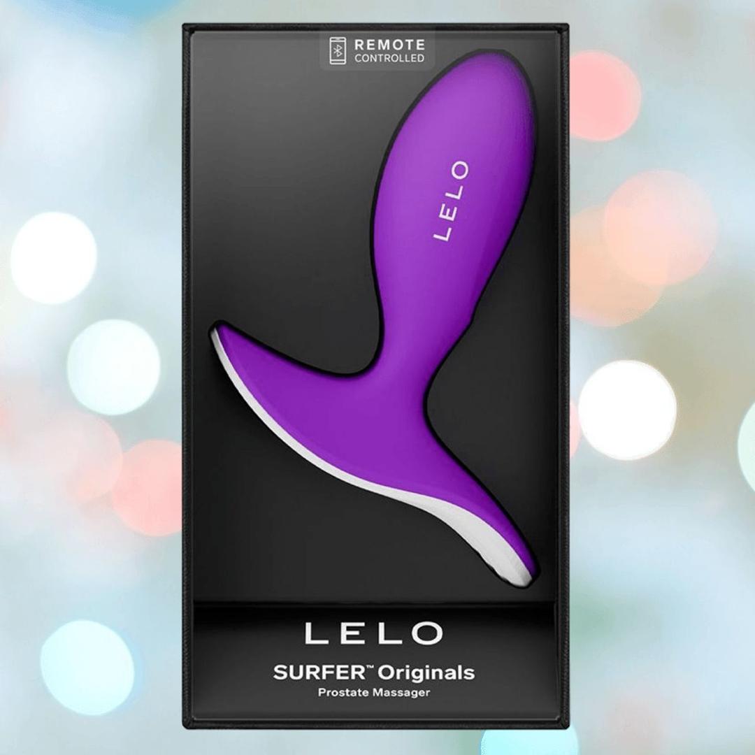 The LELO SURFER Originals Purple prostate massager is shown in sleek black packaging, featuring remote control text. The softly blurred background with light bokeh highlights the stylish LELO design.