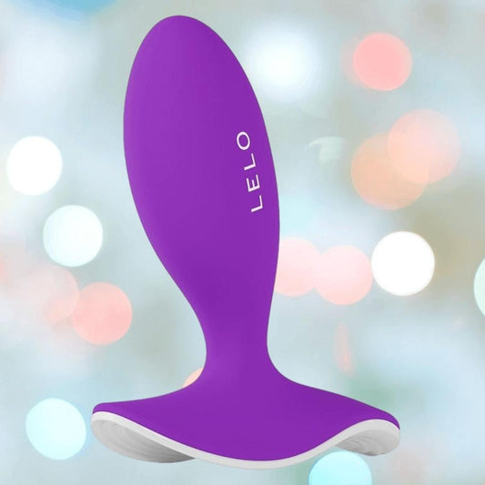 The Lelo SURFER Originals Purple is a curved, ergonomic silicone device by LELO, shown with its brand name against a blurred, colorful bokeh background. 1080