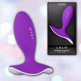 The Lelo SURFER Originals Purple by LELO is displayed beside its black packaging, which showcases the product and brand name. The scene features a softly blurred bokeh background.