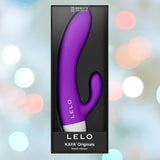 A box featuring the LELO KAYA Originals Purple rabbit vibrator with remote control, upright and set against a blurred backdrop of colorful lights.