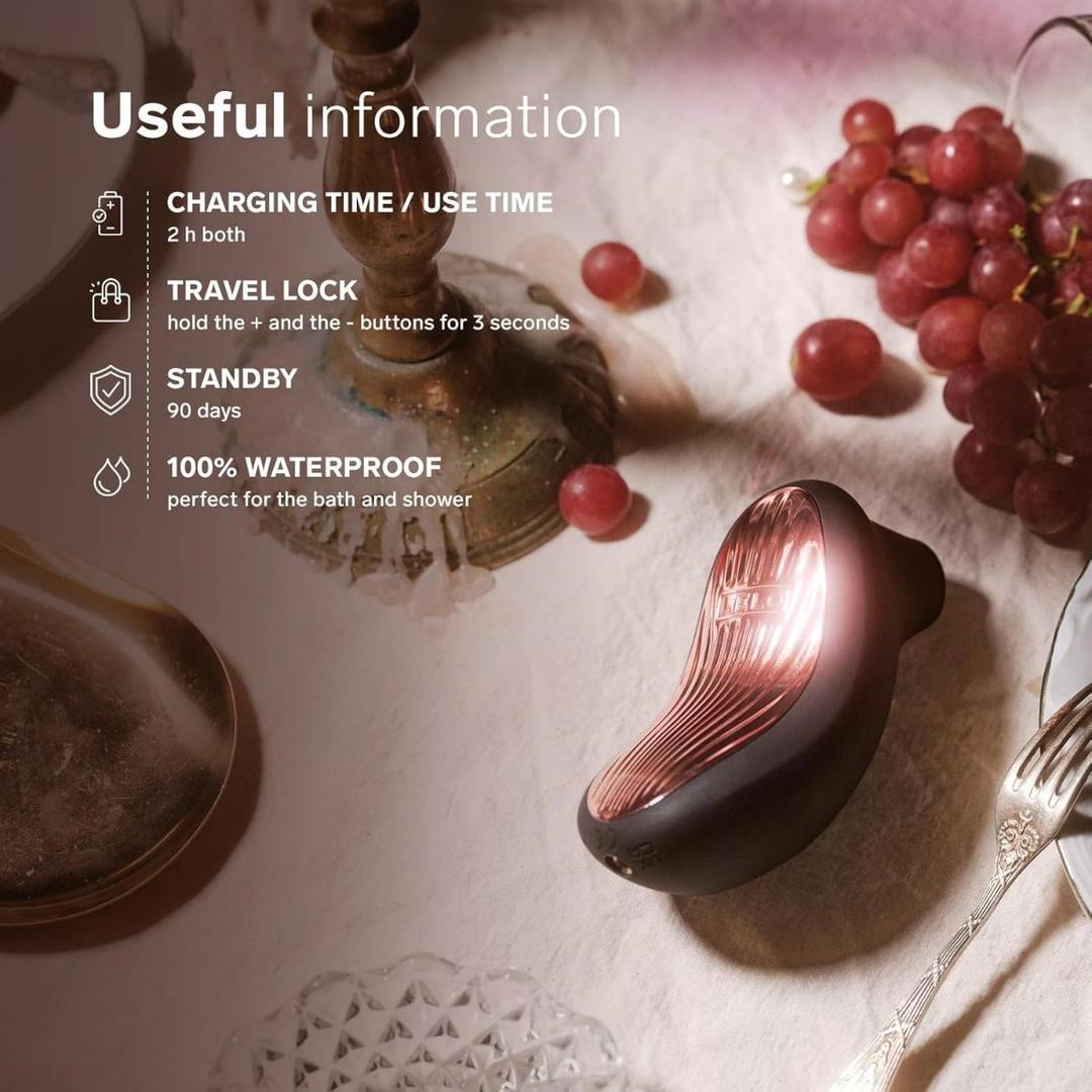 The LELO Sona 3 Cruise in black rests on a table near red grapes and a fork, with overlay text highlighting: 2-hour charge/use, travel lock, 90-day standby, and 100% waterproof for bath and shower.