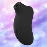 The LELO Sona 3 Cruise in black, a curved silicone device with side control buttons, is displayed against a soft, pastel purple and blue blurred background.