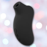 The LELO Sona 3 Cruise - Black, a handheld device by LELO made of body-safe silicone with a rounded shape and three side buttons, is set against a blurred background with pink and white bokeh lights.