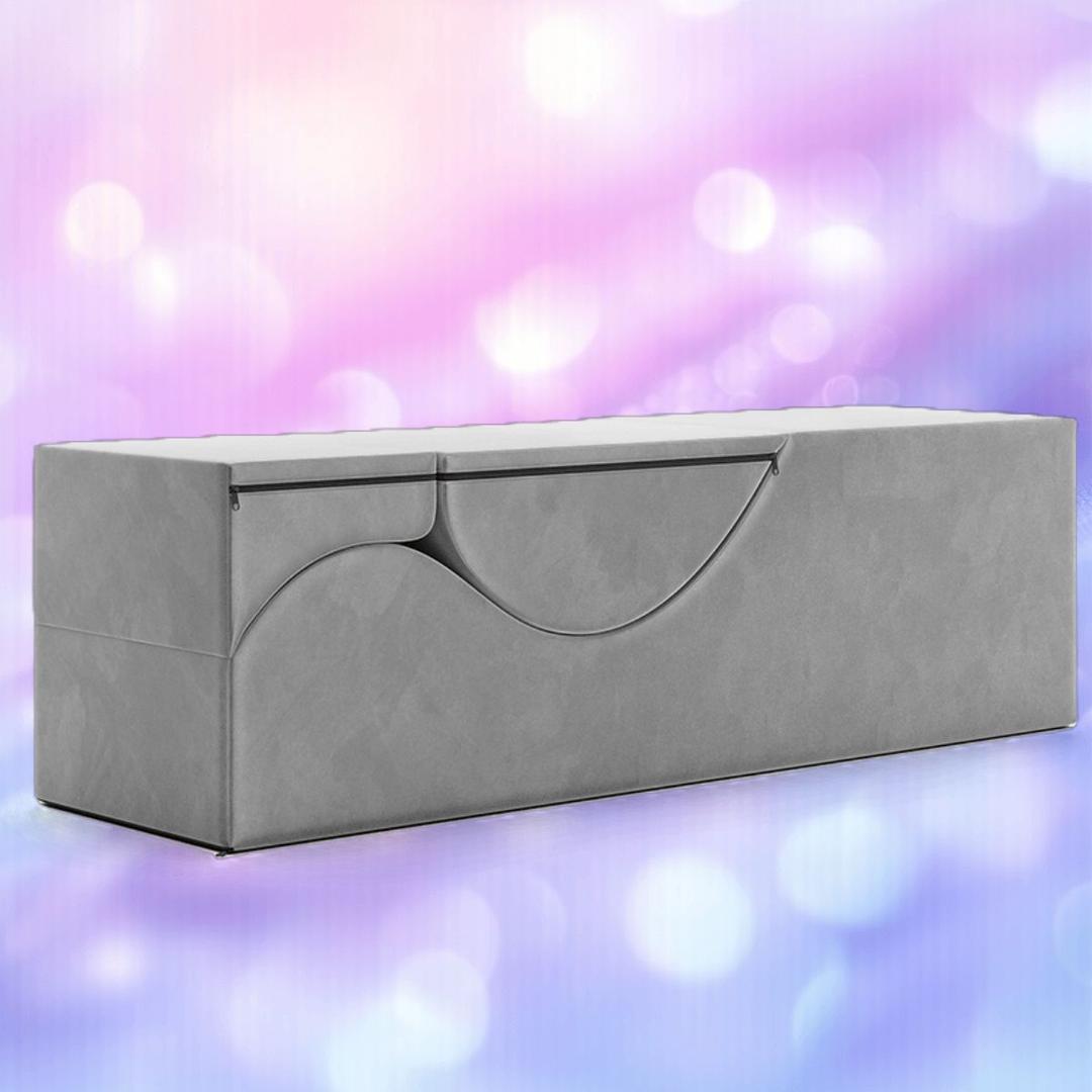 The Liberator Aria Chaise in grey by Liberator—a modern, minimalist convertible love lounge ottoman—sits against a soft pink and purple blurred background, blending stylish decor with discreet sex furniture functionality.