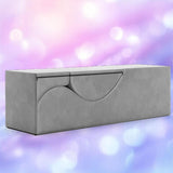 The Liberator Aria Chaise in grey by Liberator—a modern, minimalist convertible love lounge ottoman—sits against a soft pink and purple blurred background, blending stylish decor with discreet sex furniture functionality.