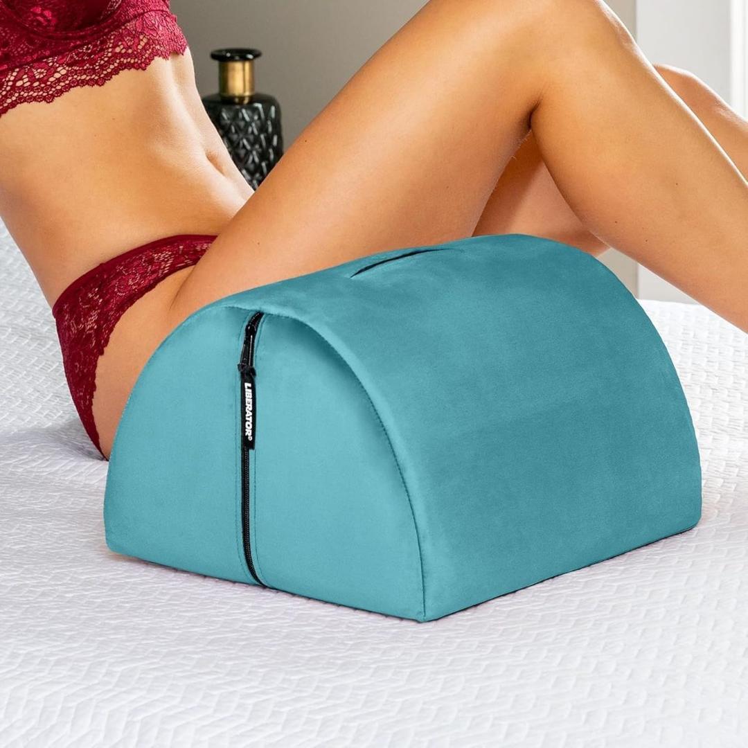 A person in red lingerie reclines on a bed, using the Liberator BonBon Microvelvet - Teal pillow by Liberator—a supportive sex toy mount with a zipper, perfect for hands-free solo play.