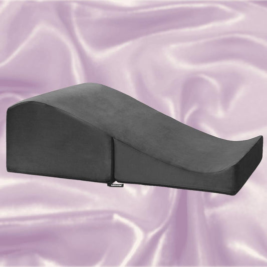 The Liberator Flip Ramp MicroVelvet in black from Liberator rests on a soft, light purple satin background, showcasing its sleek wedge-shaped design and gradual incline. 1080