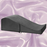 The Liberator Flip Ramp MicroVelvet in black from Liberator rests on a soft, light purple satin background, showcasing its sleek wedge-shaped design and gradual incline.