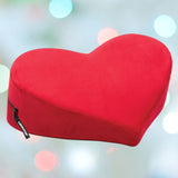 A red Liberator Heart Wedge MicroVelvet pillow by Liberator, heart-shaped with a zipper and side tag, inspired by the original design and shown against a blurred pastel light background.