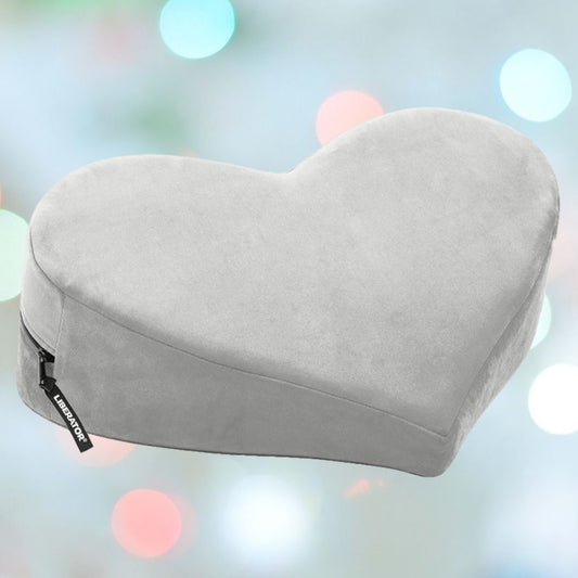 The Liberator Heart Wedge MicroVelvet - Grey by Liberator is shown against pastel lights, featuring a heart shape, soft microvelvet cover, and side zipper—ideal as a cozy derriere positioning aid or stylish home decor accent. 1080