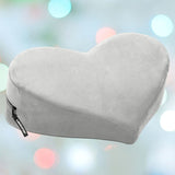 The Liberator Heart Wedge MicroVelvet - Grey by Liberator is shown against pastel lights, featuring a heart shape, soft microvelvet cover, and side zipper—ideal as a cozy derriere positioning aid or stylish home decor accent.