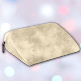 A Liberator Jaz Ibiza Collection - Natural pillow by Liberator sits on a soft-focus pastel background with pink, blue, and white light spots. Its smooth beige surface is ideal for G-spot stimulation and features a small black tag on the side.