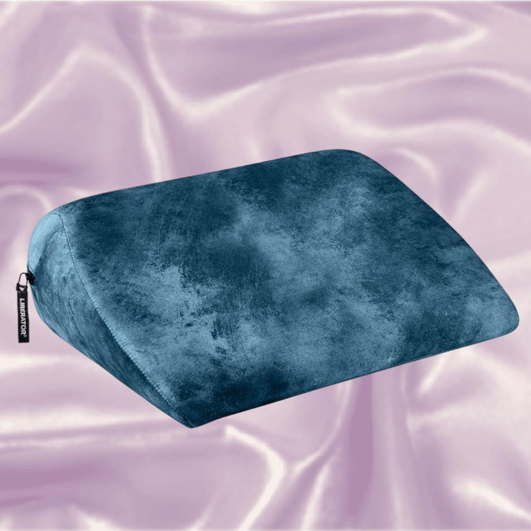 The Liberator Jaz Ibiza Collection - Ocean Blue, a wedge-shaped sex pillow by Liberator with a soft velvet texture, rests on shiny light pink satin fabric.