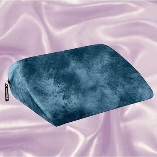 The Liberator Jaz Ibiza Collection - Ocean Blue, a wedge-shaped sex pillow by Liberator with a soft velvet texture, rests on shiny light pink satin fabric. 1080