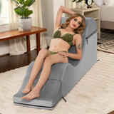 A woman in green lingerie reclines on the Liberator Aria Chaise - Grey by Liberator in a modern living room featuring wooden furniture and a nearby potted plant.
