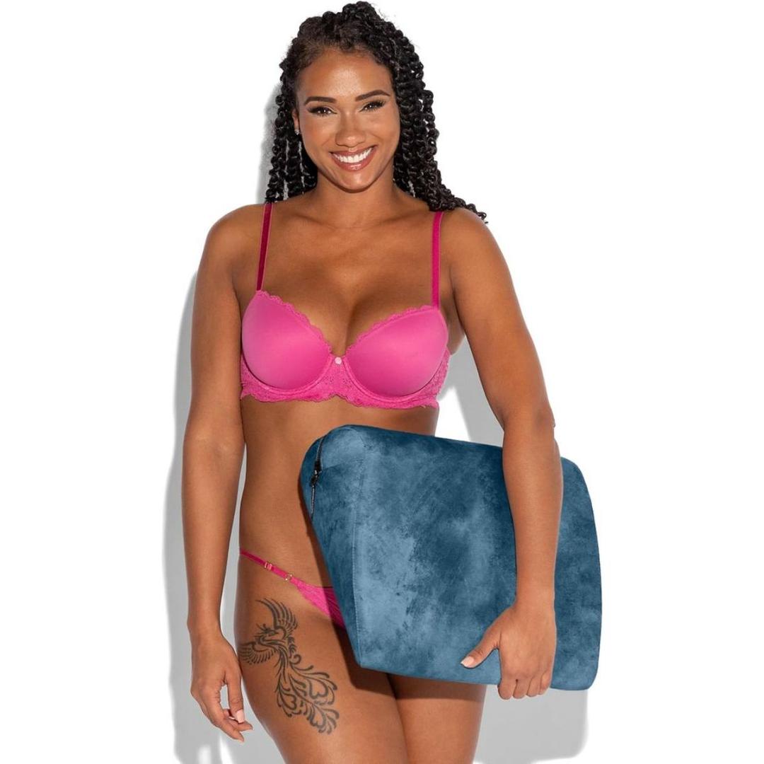 A smiling woman with a floral thigh tattoo holds the Liberator Jaz Ibiza Collection – Ocean Blue memory foam wedge cushion by Liberator, standing against a plain white background in pink bra and underwear.