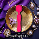 A vibrant magenta BMS Swan Sceptre Wand rests on a gold plate amid purple fabric, pearls, and flowers. Its body-safe design combines elegance with powerful vibrations. Text below reads: "THE SWAN SCEPTRE.